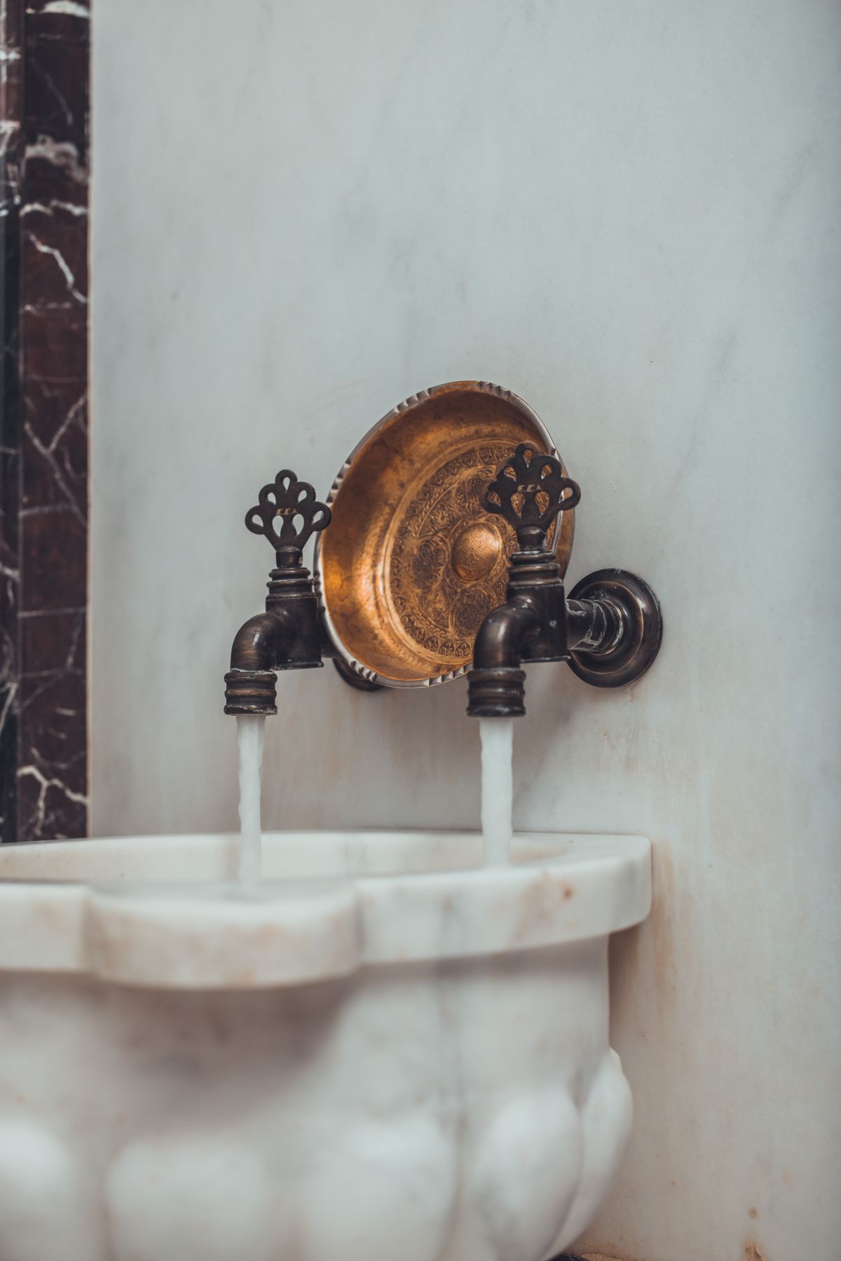 Wall-mounted brass tap running clean water over a stone basin